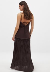 Braunes Maxikleid mit einem geschichteten, plissierten Rock und einem taillierten Oberteil. Verfügt über dünne Träger und einen tiefen Rücken mit einer Krawattenverschluss. Leichtes Material.