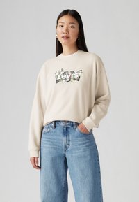 Felpa color crema con logo floreale di Levi's sul davanti. Abbinata a jeans a vita alta blu chiaro, che mostrano un fit rilassato.