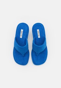 Sininen pyyhkeentuntuinen flip-flop-malli, jossa on thong-muotoilu. Ominaisuuksiin kuuluvat pehmeä pinta, tasainen pohja ja etiketti sisäpohjassa.
