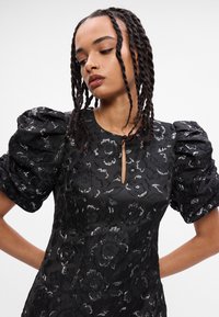 Crna haljina s napuhanim kratkim rukavima, uzorkom cvjetova, detaljem u obliku ključanice na dekolteu i glatkom satenskom završnicom.