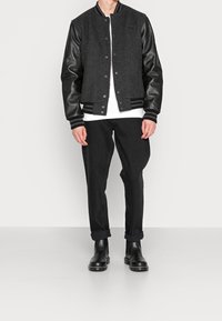 Black wool-blend bomber jacket with leather sleeves, ribbed cuffs and hem, worn with black jeans and black ankle boots.
