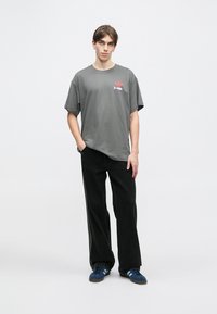 Šedé bavlněné tričko s kulatým výstřihem a krátkými rukávy, zdobené barevným grafickým potiskem; doplněno volnými černými manšestrovými kalhotami.