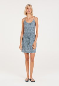 Blaue gemusterte Sommerkleid mit schmalen Trägern, tailliertem Schnitt und lockerer Passform. Kombiniert mit blauen Flip-Flops. Einfaches geometrisches Design.