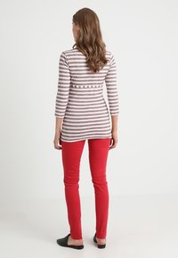 Top de rayas de manga larga con cintura ajustada, combinado con pantalones ajustados rojos y zapatos negros tipo slip-on. Tejidos suaves y diseño sencillo.