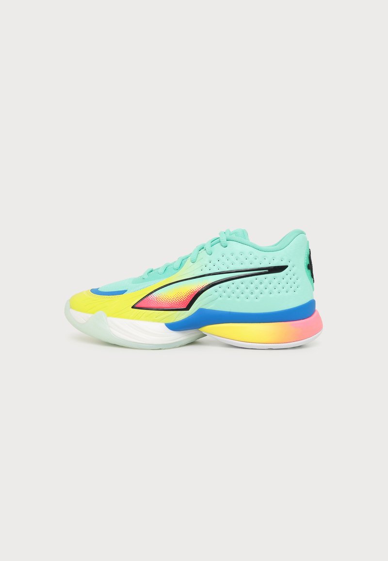 Πλάγια όψη πολύχρωμου αθλητικού sneaker με τιρκουάζ επάνω μέρος, κίτρινη μύτη, μαύρο λογότυπο και μοβ, κίτρινη και ροζ βαθμιδωτή σόλα σε λευκό φόντο.