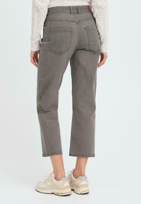 Jeans gris de corte cropped y media altura con un ajuste relajado, que cuentan con bolsillos traseros y una cinturilla cosida. Combinados con zapatillas de color claro.