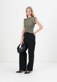 Top tricotat de culoare verde măsliniu cu mâneci scurte și închietori decorative, asociat cu blugi negri cu talie înaltă și o geantă de mână neagră. Pantofi negri cu bot ascuțit.