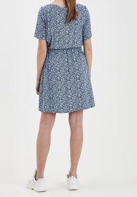 Modrá květinová šaty s krátkými rukávy, nařaseným pasem a délkou nad kolena. V kombinaci s bílými teniskami pro neformální vzhled.