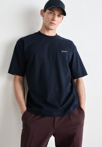 Βαμβακερό μπλουζάκι σε ναυτικό μπλε χρώμα με κοντά μανίκια, με μικρό κόκκινο και λευκό λογότυπο "BOSS" στο αριστερό στήθος. Με ομαλή υφή.