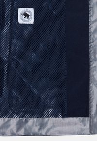 Tessuto blu navy con texture a rete su un lato e materiale liscio dall'altro; presenta una piccola etichetta logo bianca. I bordi hanno una rifinitura argentata.