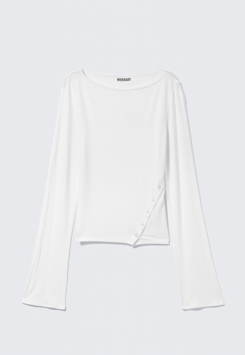 Camicia bianca a maniche lunghe con scollo a barca e bottoni a pressione diagonali sul lato inferiore destro, etichetta del marchio "Weekday" all'interno del colletto.