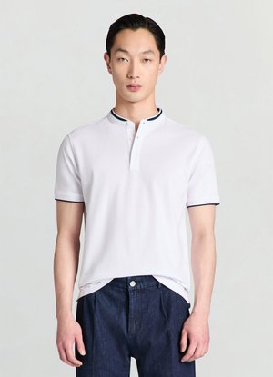 Polo bianca con colletto con accenti scuri, maniche corte e una patta con due bottoni. Indossata con pantaloni di denim scuro.