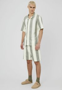 Ensemble composé d'une chemise à manches courtes et d'un short en crème clair avec des rayures verticales vertes. Tissu doux avec une coupe décontractée et une fermeture à boutons.