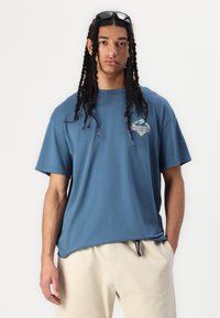 T-shirt en coton bleu à manches courtes et col rond, avec un logo graphique multicolore sur la poitrine et une coupe décontractée.