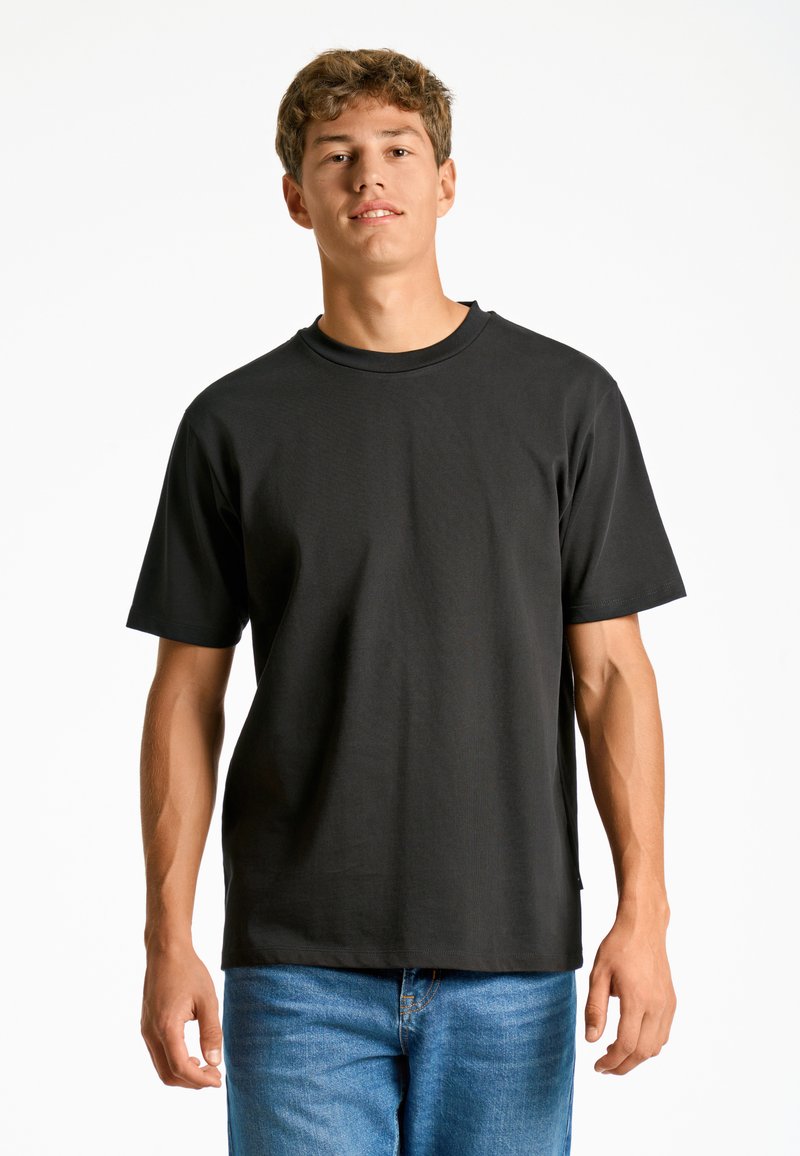 T-shirt nero a maniche corte in un fit rilassato, realizzato in tessuto morbido con design a girocollo. Il modello lo abbina a jeans in denim blu.