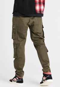 Gröna cargobyxor med avslappnad passform, som har flera sidofickor och förstärkta knäområden, matchade med stiliga svarta och rosa sneakers.