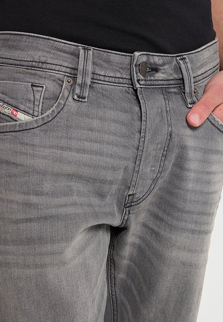 Graue Jeans aus Denim mit klassischem Fünf-Taschen-Design, das eine subtile verblasste Textur und Metallknopf-Beschläge aufweist.