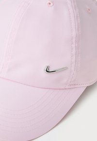 Rozā beisbola cepure, izgatavota no viegla auduma ar izliekto malas, ar šūtām detaļām un metāliski sudraba Nike logo sānos.