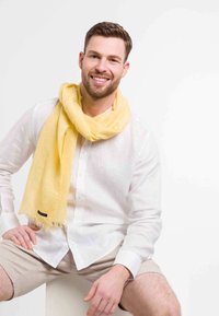 Yellow lightweight scarf with fringe detail, draped around the neck, worn over a white button-up shirt, featuring short sleeves and a casual fit.