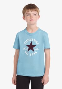 Svijetloplava pamučna majica kratkih rukava s velikim bordo zvjezdanim logotipom i bijelim tekstom "Converse Chuck Taylor All Star" oko njega.