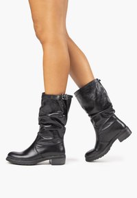 Musta nahkaiset keskivartalon saappaat, joissa on rennon muotoilun lisäksi sivuunkiristyskoriste ja teksturoitu pinta. Kestävä kumipohja, jossa on hillitty korko.