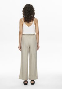 Pantalons larges en lin beige avec une taille élastique, associés à un haut sans manches blanc avec un dos en V. Sandales à plateforme noires.