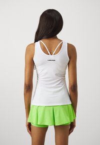 Hvit atletisk tank topp med tynne stropper, med en logo på baksiden; kombinert med et lyst grønt plissert skjørt. Glatt tekstur.