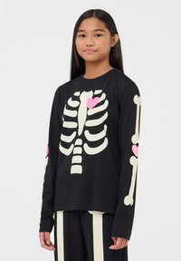 Czarna koszula z długim rękawem z białym nadrukiem szkieletu oraz różowymi akcentami w kształcie serca na klatce piersiowej i rękawach. Okrągły dekolt, miękki materiał bawełniany.