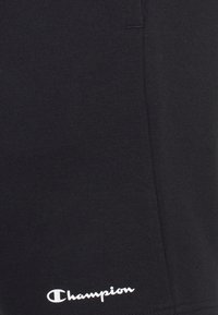 Mustat puuvillashortsit, joissa on sileä pinta, ja vasemmassa alareunassa on valkoinen brodeerattu "Champion"-logo.