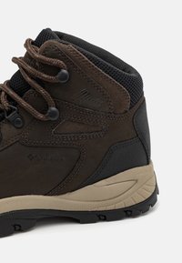 Hnědé a černé voděodolné hiking boty s polstrovaným límcem, silnou béžovou podešví a hnědými tkaničkami provlečenými kovovými očky.