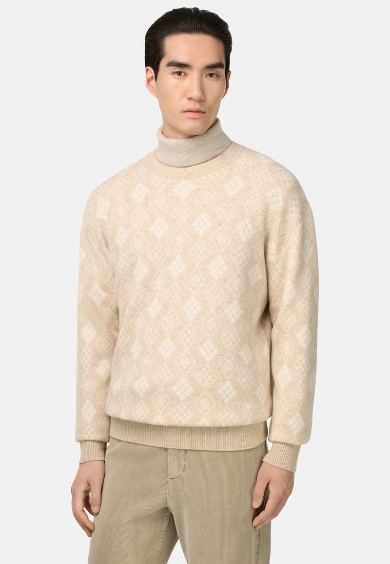 Pull à col roulé beige à motifs avec un design en diamants, fabriqué en matériau tricoté doux. Il présente des poignets et une taille côtelés, associé à un pantalon clair.