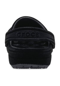 Zwarte Crocs-schoenen met een gladde, gestructureerde band en open achterkant. De rubberen zool heeft kleine antislipbulten voor grip.