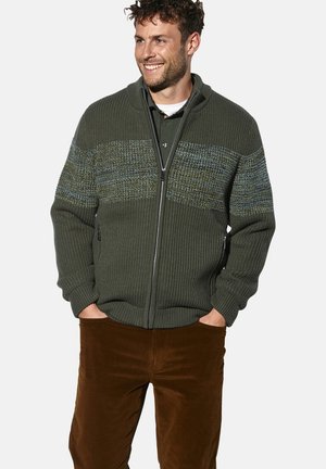 Grüne Strickjacke mit Reißverschluss, die strukturierte horizontale Streifen in Blau und Grün aufweist. Kombiniert mit braunen Cordhosen.
