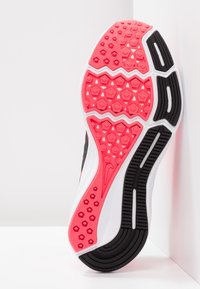 Semelle de chaussure de sport noire et rose présentant un motif de grip texturé, une forme arrondie et des accents blancs contrastants le long des bords.