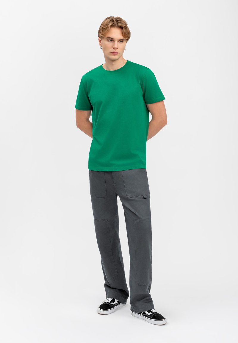 T-shirt vert à manches courtes avec un col rond, assorti à un pantalon large gris avec des poches fonctionnelles, porté avec des baskets basses noires.