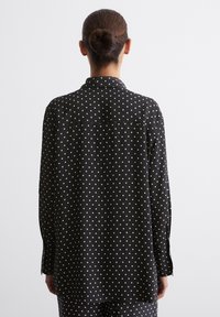 Langarmhemd in Schwarz mit weißen Polka-Dots, mit einem kragenförmigen Ausschnitt und einer geknöpften Rückseite, aus glattem Stoff gefertigt.