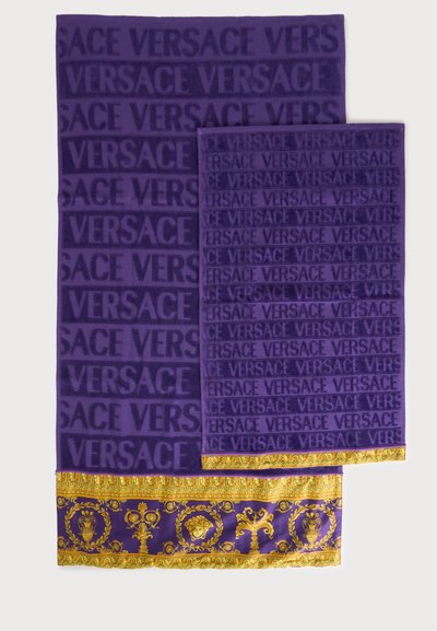 Deux serviettes violettes avec un texte répété "VERSACE" et une bordure décorative dorée et violette présentant des motifs classiques et des têtes de Méduse.