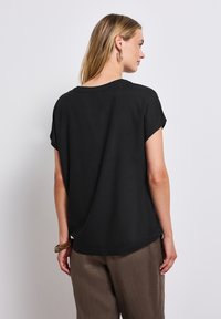 Černý krátký rukáv top s volným střihem a kulatým výstřihem, v kombinaci s béžovými, volnými kalhotami. Hladká textura, minimalistický design.