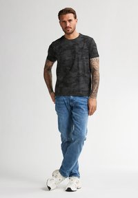 Černé tričko s texturovaným, vzorovaným designem, kombinované se světle modrými džíny a bílými sportovními botami. Mezi hlavními rysy jsou krátké rukávy a kulatý výstřih.