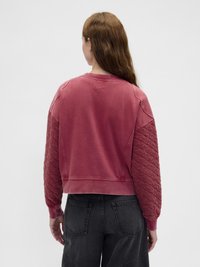 Sudadera rosa con textura acolchada en las mangas, cuello redondeado y puños acanalados, combinada con vaqueros oscuros. Vista trasera mostrada.