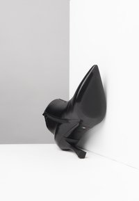 Bota de tacón alto de cuero negro con punta afilada, que cuenta con un cierre de cremallera en el tobillo y una suela texturizada para mayor agarre.