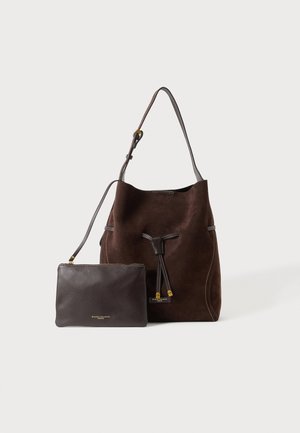 Dunkelbraune Wildleder-Bucket Bag mit verstellbarem Schulterriemen und passendem dunklem Leder-Reißverschlussbeutel vor hellem Hintergrund.