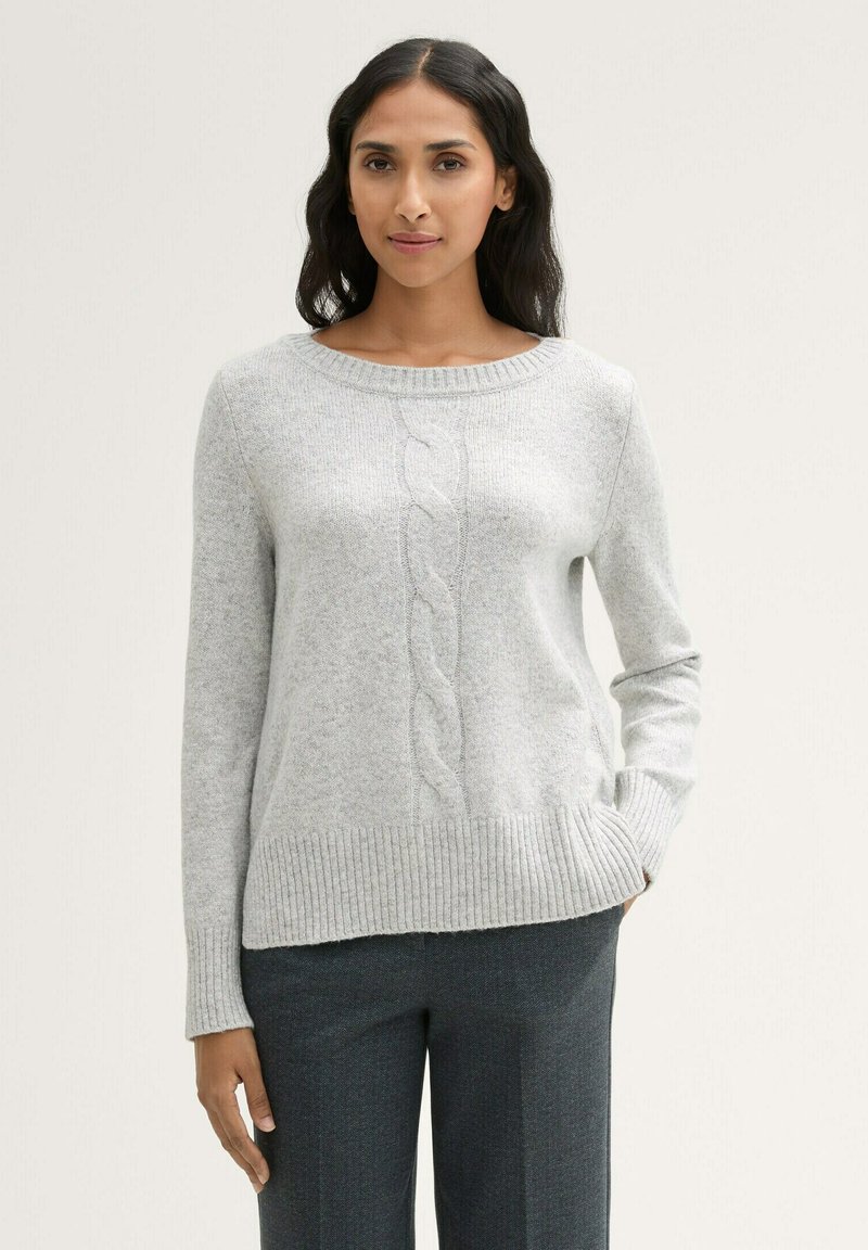 Helle graue Strickjacke mit rundem Halsausschnitt, geripptem Saum und Zopfmuster-Details auf der Vorderseite. Kombiniert mit dunkelgrauen, maßgeschneiderten Hosen.