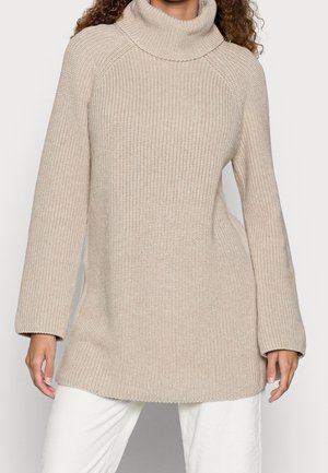 Beige neulekauluspaita, jossa on pitkät hihat, ribbikuviointi ja rento istuvuus. Helma on hieman pidempi takana.