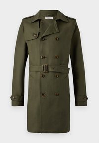 Long trench-coat vert olive à double boutonnage avec poignets boutonnés, ceinture à la taille, épaulettes et poches latérales.