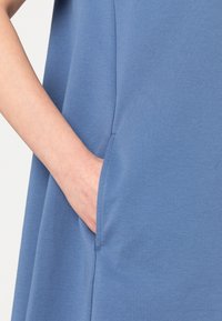 Niebieska tkaninowa odzież z boczną kieszenią. Gładka, miękka struktura i luźny krój. Materiał wydaje się elastyczny i lekki.