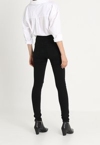 Černé skinny džíny s vysokým pasem, doplněné volnou bílou košilí na knoflíky. Outfit je doplněn černými botami na podpatku do poloviny kotníku.