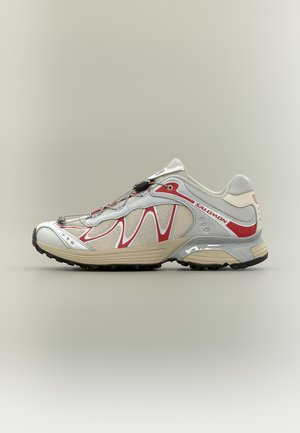 Chaussure de sport Salomon blanche et rouge avec semelle beige, panneaux latéraux en mesh et fermeture à lacets rapides, présentée de profil sur un fond neutre.