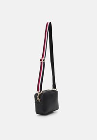 Borsa a tracolla nera in pelle con forma rettangolare, caratterizzata da una tracolla regolabile a strisce rosse, bianche e nere e accenti in metallo dorato.