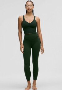 Mørkegrøn atletisk tanktop med brede stropper og V-udskæring, parret med matchende højtsiddende leggings. Glat tekstur, tætsiddende design.